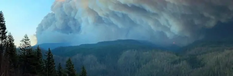 A column of smoke over a forested hills