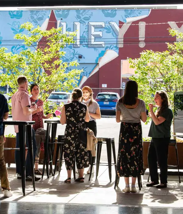 Six people talking around cocktail tables in an outdoor patio.