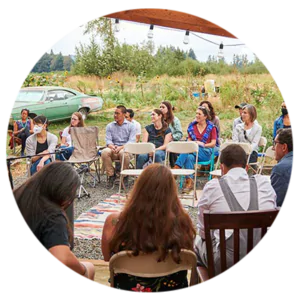 A photo of a dozen people sitting and listening to a small panel of speakers