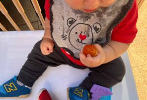 close up of toddler, seated, eating a cherry tomato