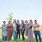 Group of eight people standing close together on a farm, smiling at camera