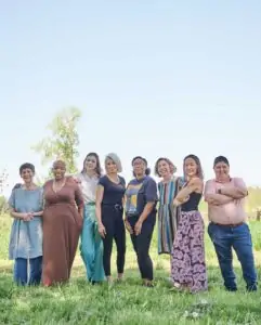 Group of eight people standing close together on a farm, smiling at camera