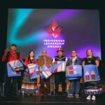 Dramatically lit stage with six people on stage on stage, backdrop screen reads Indigenous Leadership Awards