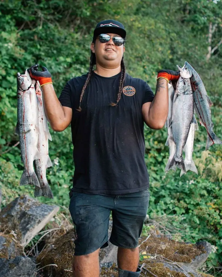 Person holding abundant fish, smiling at camera, long braids, in nature