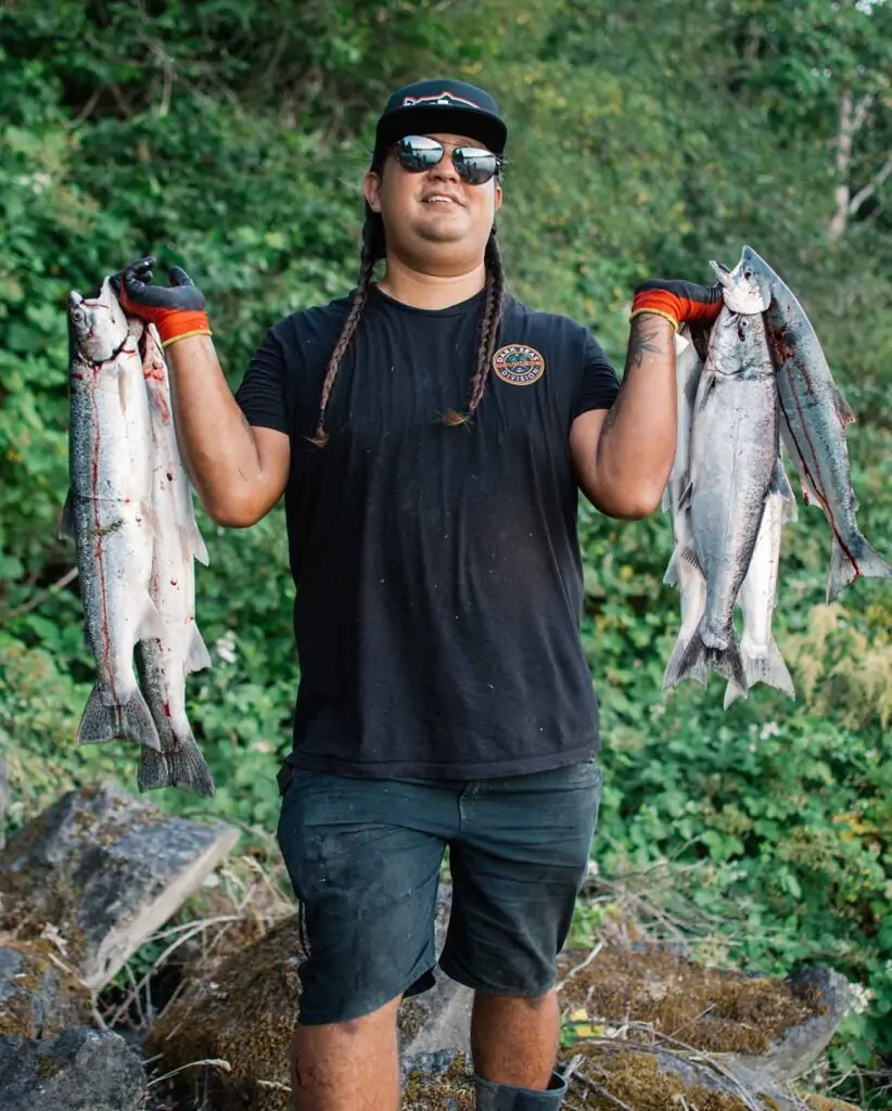 Person holding abundant fish, smiling at camera, long braids, in nature