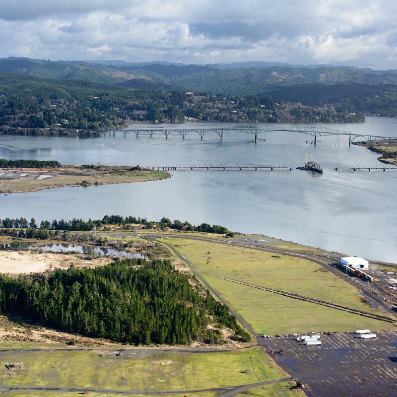 An aerial view of a coastal bay with a green bridge and forested hills in the background