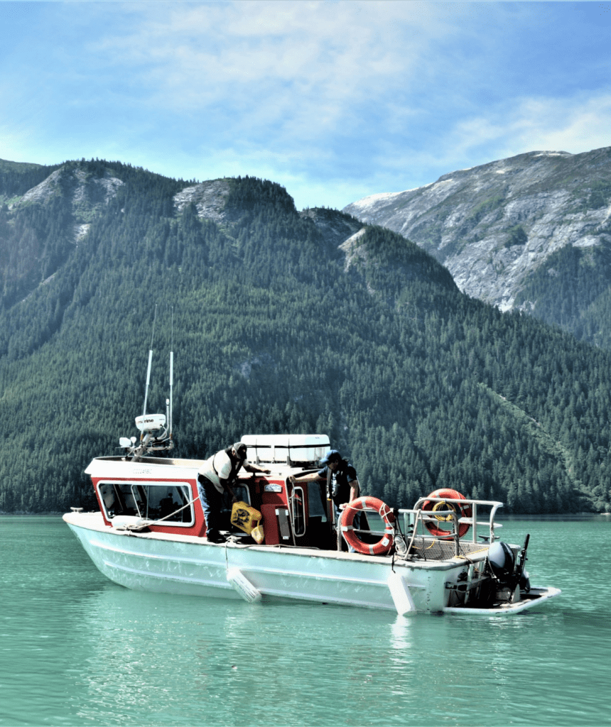 A boat on milky aqua water, with forested hills in the background