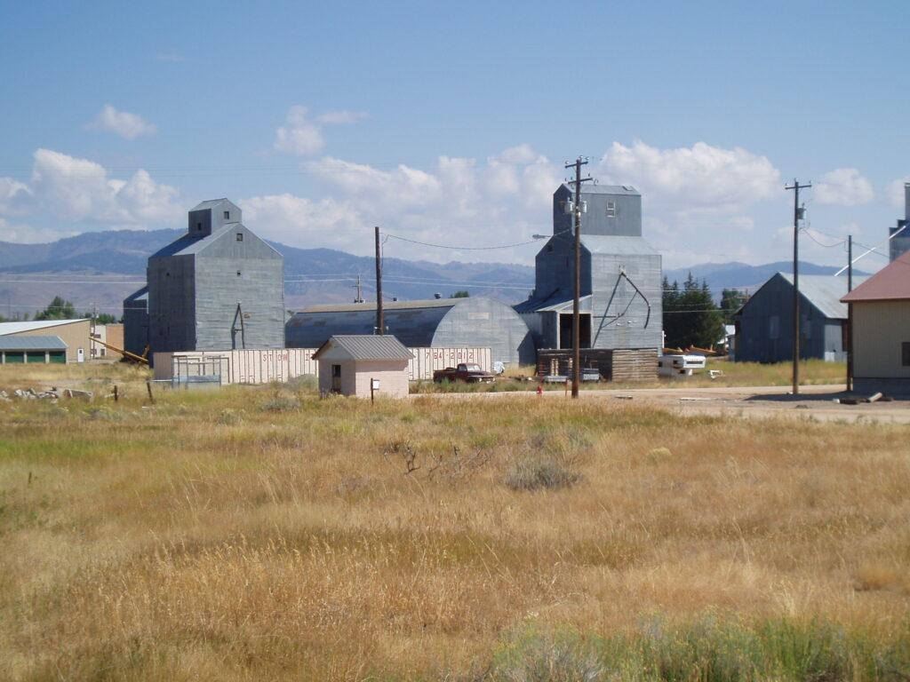 Wooden granary bunched with several small buildings, surrounded by high desert grasses with mountains in the distance
