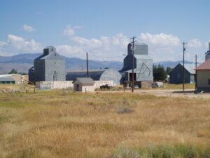 Wooden granary bunched with several small buildings, surrounded by high desert grasses with mountains in the distance