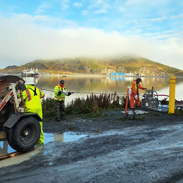 Three people wearing brightly colored uniforms install wires, against a backdrop of a clouded mountain reflected in clear water.