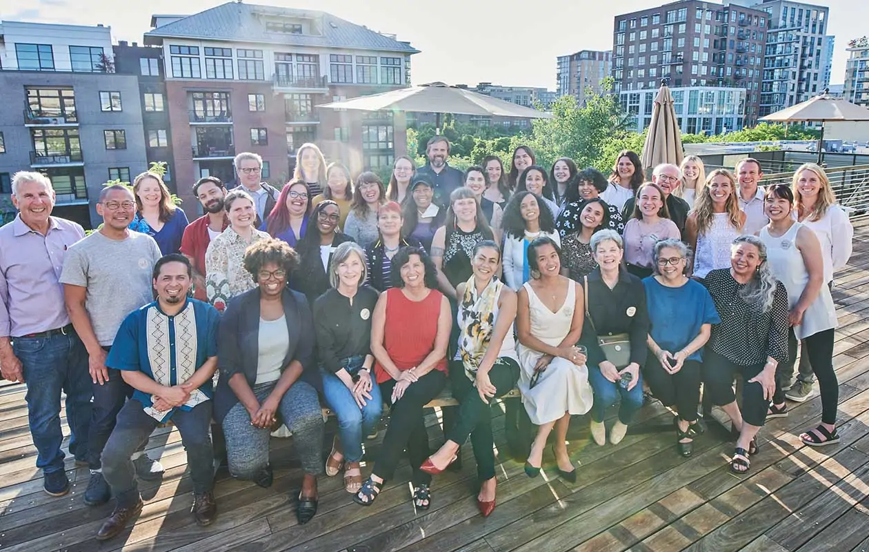 A group of three dozen adults, some seated and some standing, posing for a group photo on a rooftop terrace