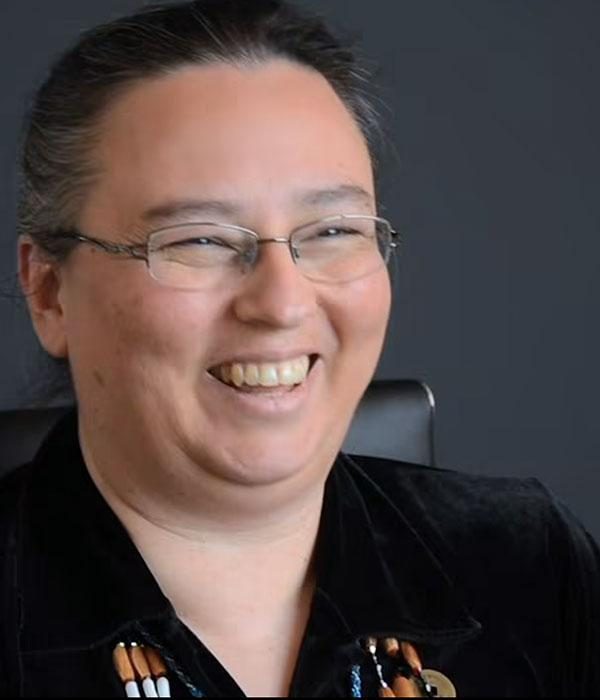 close up of a person wearing glasses, beaded necklace, laughing