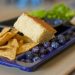 A blue school lunch tray showing corn chips and salsa, cornbread, fresh blueberries, and salad greens.