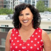 person smiling with shoulder length dark hair and red polka-dotted top