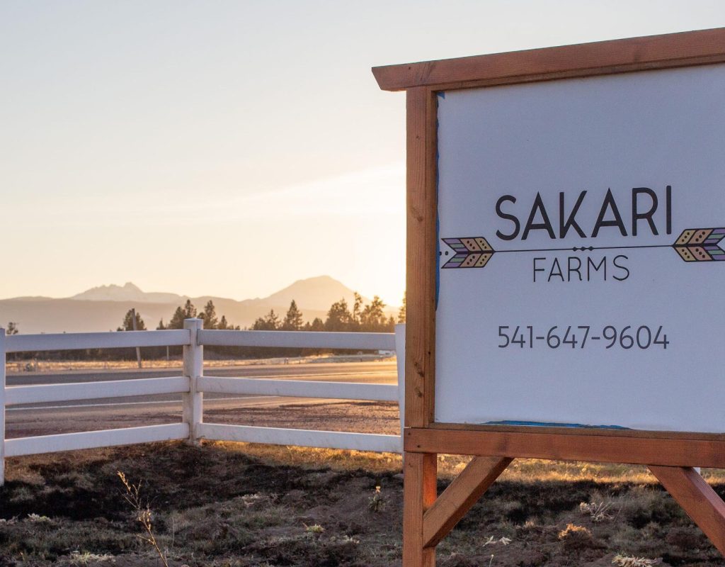 A photo of a sign for Sakari Farms with mountains in the background during sunset