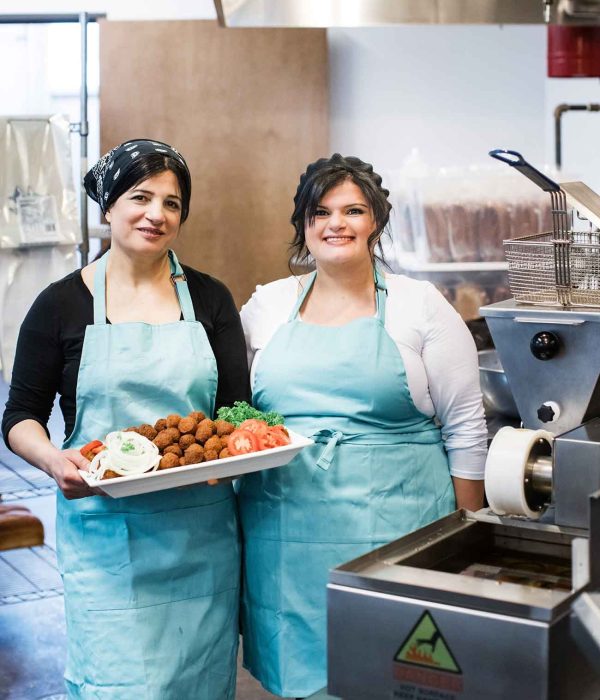 A photo of two women in an industrial kitchen smiling at the camera