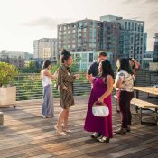 small group of event attendees talk on sunlit rooftop terrace