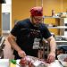 A person wearing a red bandana and glasses prepares deer meat in a community center's kitchen