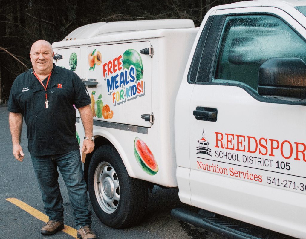 Man stands in front of white truck that says "free meals for kids"