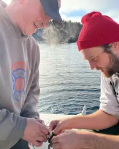 Two people on a small boat facing each other as they work on tying a knot in rope